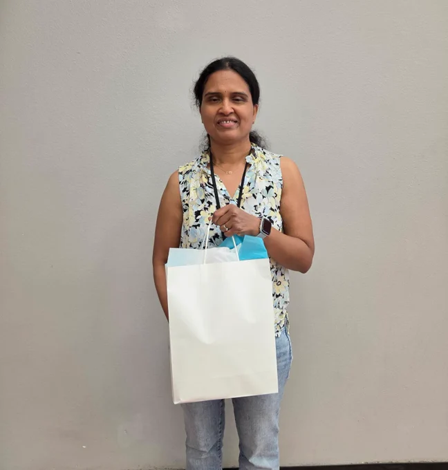 A smiling woman in a floral blouse holding a white shopping bag.