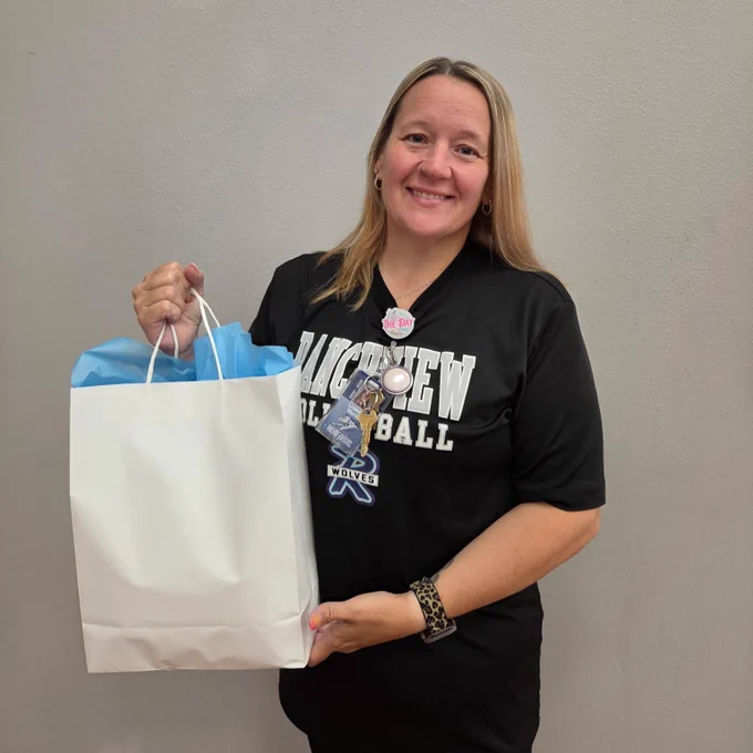 A smiling woman in a black shirt holding a white shopping bag.