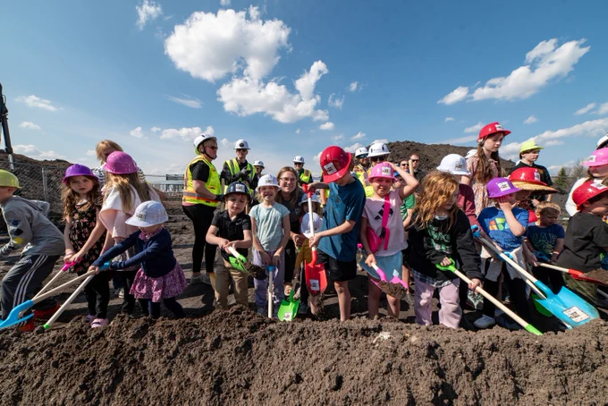 Children and PCL Construction representatives take part in a children’s museum groundbreaking in Grand Forks, North Dakota, holding colorful shovels at the construction site.
