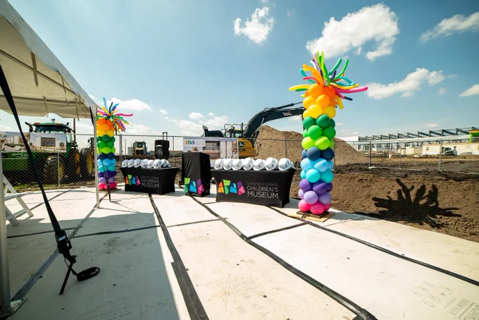 PCL Construction event setup at a children’s museum groundbreaking in Grand Forks, North Dakota, featuring branded tables, hard hats and colorful balloon columns.
