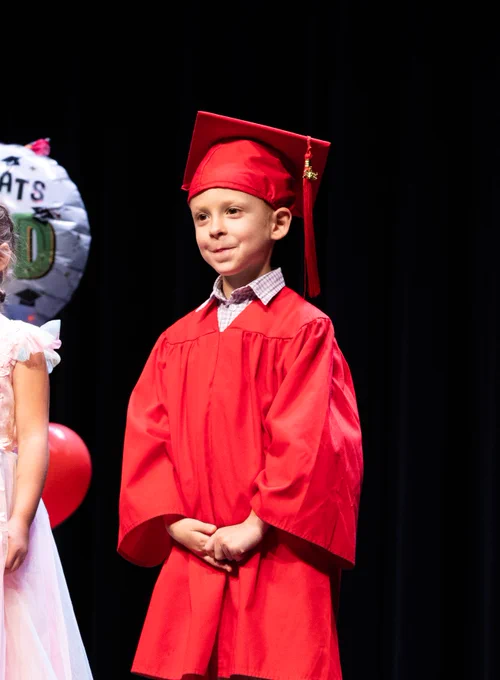 A PreK graduate stands and smiles at the crowd as he enters the stage.