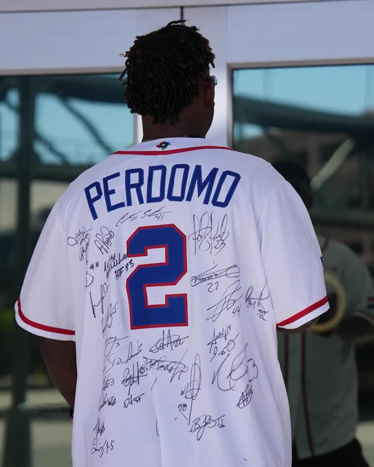 Geraldo Perdomo walking into the ballpark wearing a white Team Dominican Republic jersey with signatures on the back of many of his Team DR teammates.