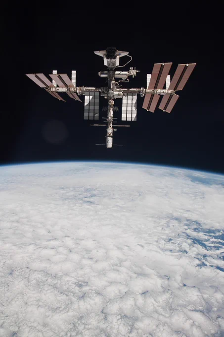 The International Space Station with the Endeavour orbiter docked is backdropped by the blackness of space in the top half of this photo. A portion of the Earth, covered in clouds, makes up the lower half of the photo.