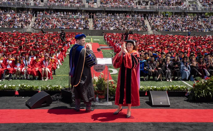 I am on stage at the Stony Brook University graduation. I am next to Provost Carl Lejuez. The gradauting class of 2026 is behind me. The stadium is filled with audience members in attendance. 