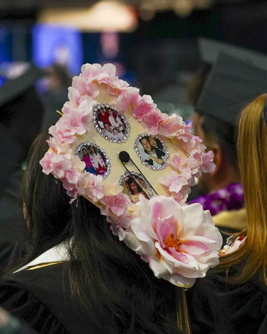 A graduate cap is decorated with pink flowers and photos of people.