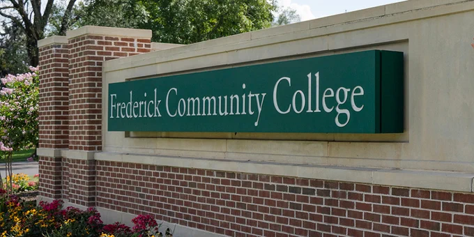 Brick and stone sign for Frederick Community College surrounded by colorful flowers and green grass under a partly cloudy sky.