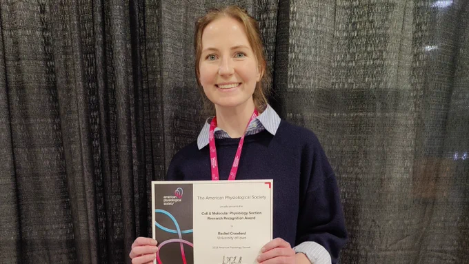 A University of Iowa graduate student smiles while holding a research recognition award certificate from the American Physiological Society at the 2026 American Physiology Summit.
