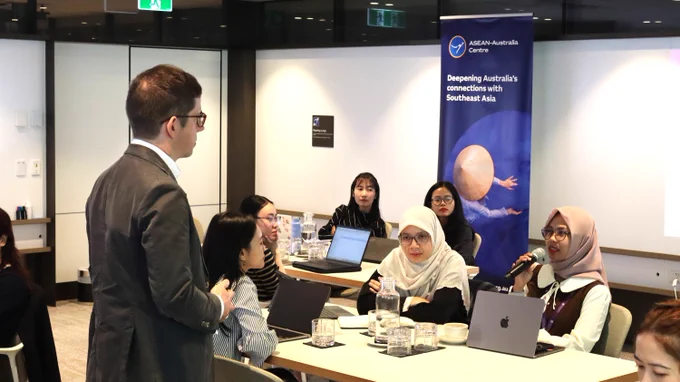 A group of participants engaged in a discussion around a conference table with laptops and documents in a modern conference setting.