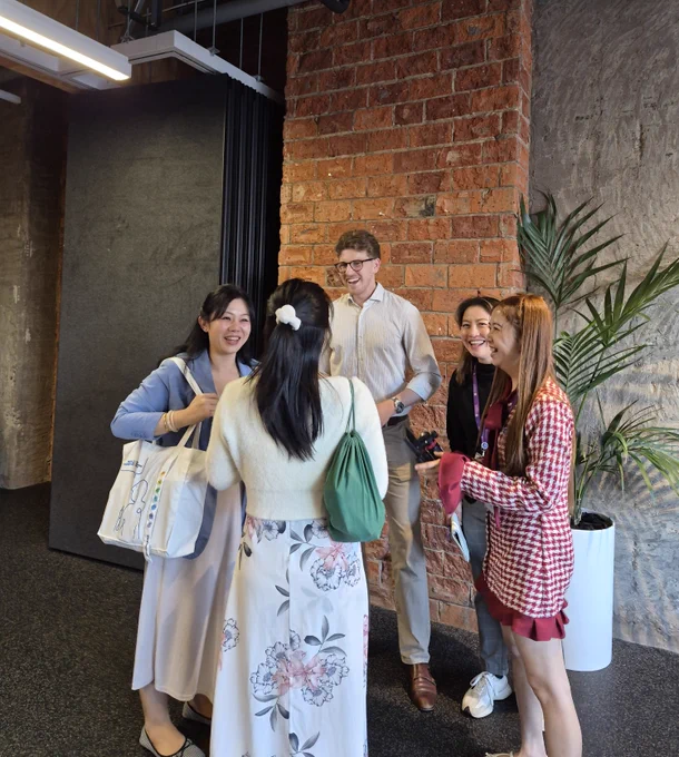 Group of participants and experts engaged in conversation, smiling and laughing inside a modern office with exposed brick walls and industrial decor.