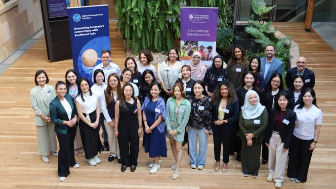 Group photo of participants and program staff indoors on wooden flooring with banners about international development behind them.