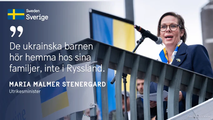 Maria Malmer Stenergard står vid en mikrofon med en ukrainsk flagga i bakgrunden. Över bilden står citatet "De ukrainska barnen hör hemma hos sina familjer, inte i Ryssland".