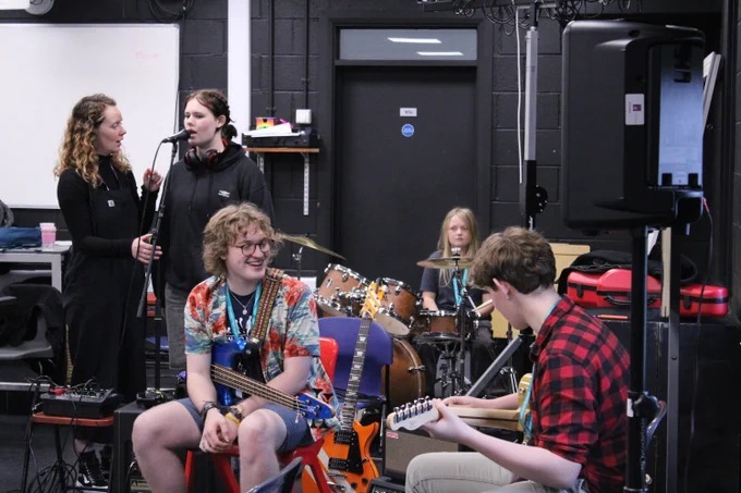 Group of young musicians rehearsing in a studio with guitars, drums, and microphones around them.