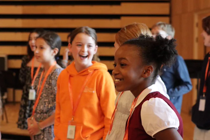 Group of children standing indoors wearing lanyards, engaged in an activity in a wooden-paneled room.
