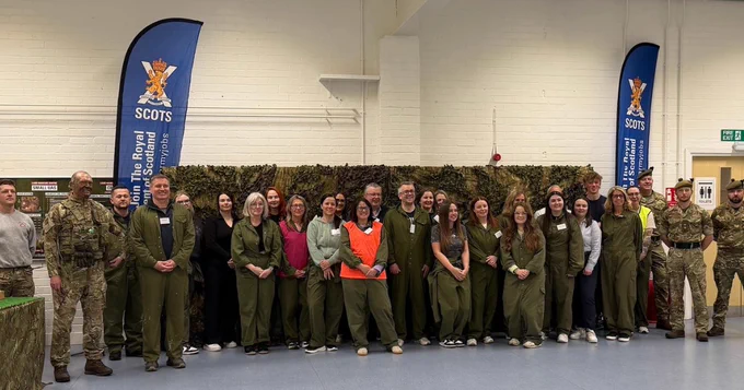 Twenty-nine people in front of a camouflaged wall.