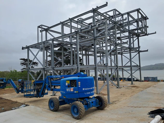 Photo of a large steel frame with a scissor lift in front of it.