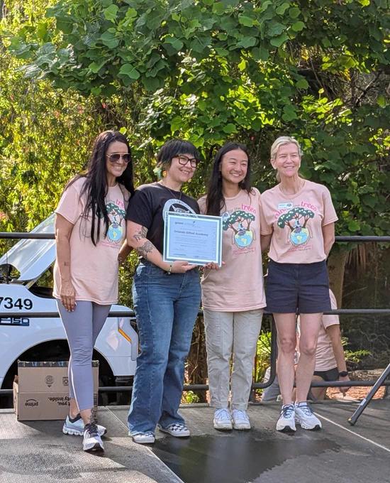 Four individuals stand on a stage, one holding a certificate for "Orlando Gifted Academy" and wearing shirts that say "run for the trees."