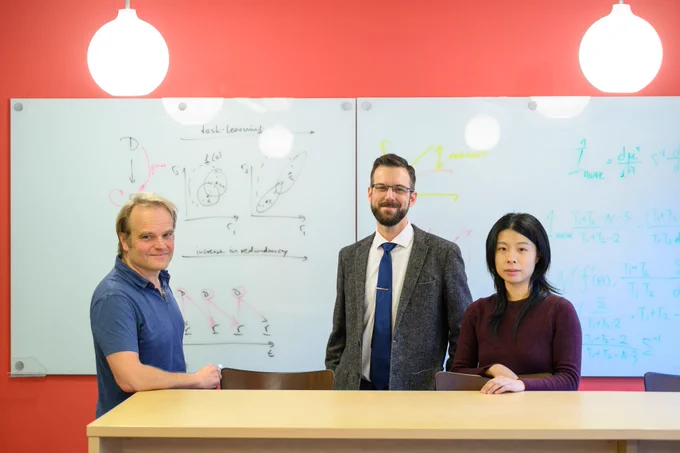 three people stand together in front of white board on red wall
