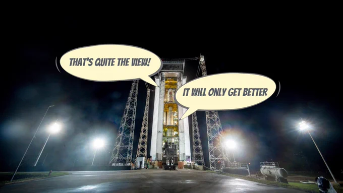 A photo showing a rocket launch pad at night. At the centre of the image is a tall rectangular cream-coloured building, with a thin white rocket inside. Platforms at various heights give people access to different parts of the rocket. The building is surrounded by metal pylons. Two speech bubbles read 'That's quite the view!' and 'It will only get better.'