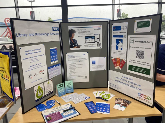 NHS Library and Knowledge Services conference stand showcasing resources including DynaMed, evidence search support, audiobooks and KnowledgeShare, with promotional materials displayed on the table.
