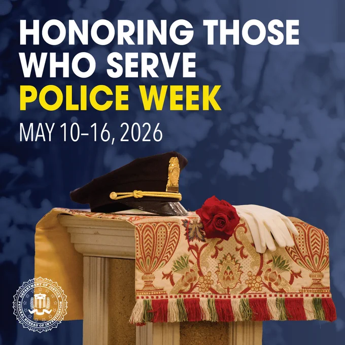 A police officer's hat, white gloves, and a red rose rest on a decorated cloth over a pedestal, honoring Police Week May 10-16, 2026.