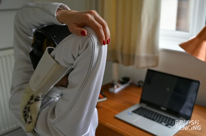 A fencer sitting in front of a laptop stretches.