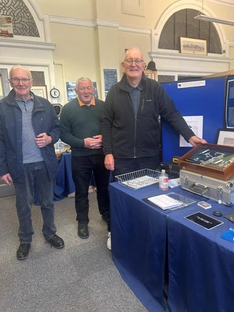 Three elderly men standing together at a table displaying items at the Coventry police museum