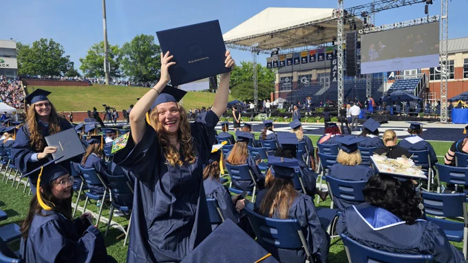 A graduate holding her degree cover over her head and smiling.