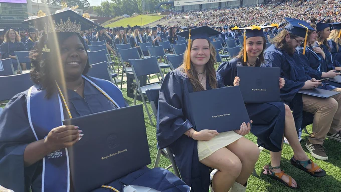 Graduates smiling and holding degree covers that say Georgia Southern University.