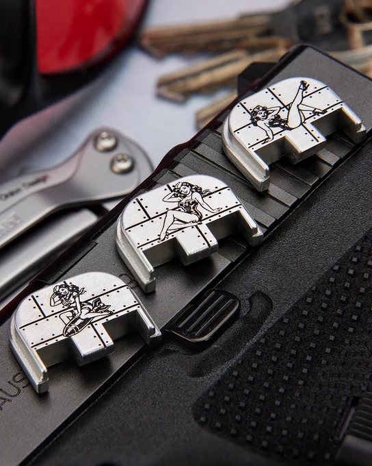 Engraved rear plates and pistol accessory featuring detailed pin-up girl artwork in a close-up desk setup.
