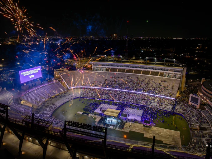 Aerial view of TCU's stadium filled with people. Fireworks light up the night sky. 