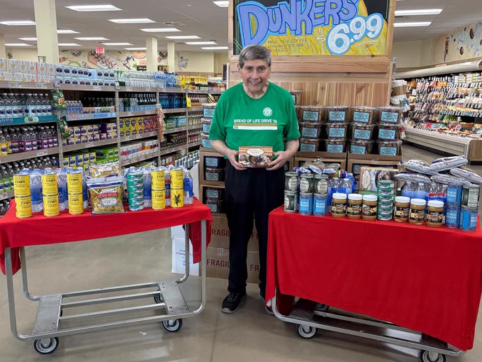 An individual in a green shirt holds a packaged food item, surrounded by promotional tables showcasing different grocery products in a well-lit store.