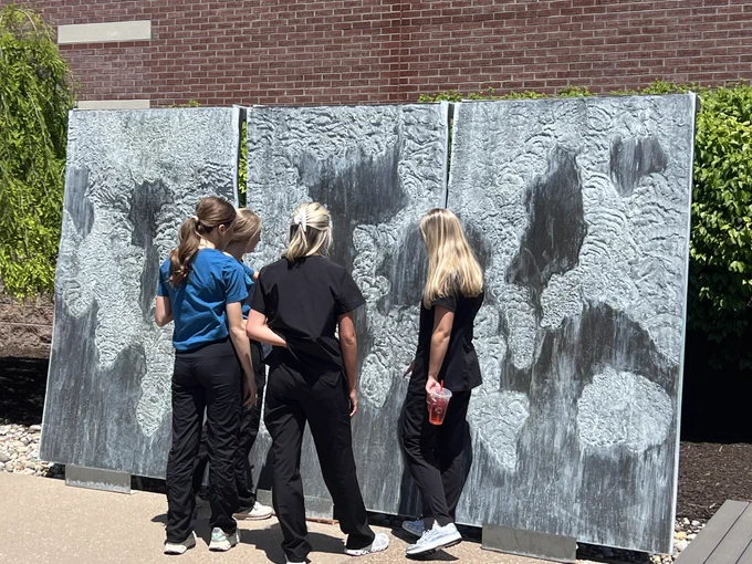 A group of people standing in front of a large outdoor mural or wall display depicting images honoring the 9/11 memorial.