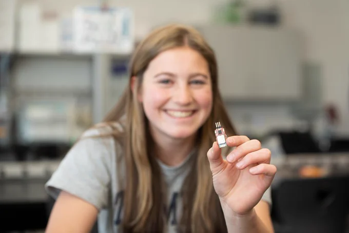 A student smiles in science class while holding a computer chip.