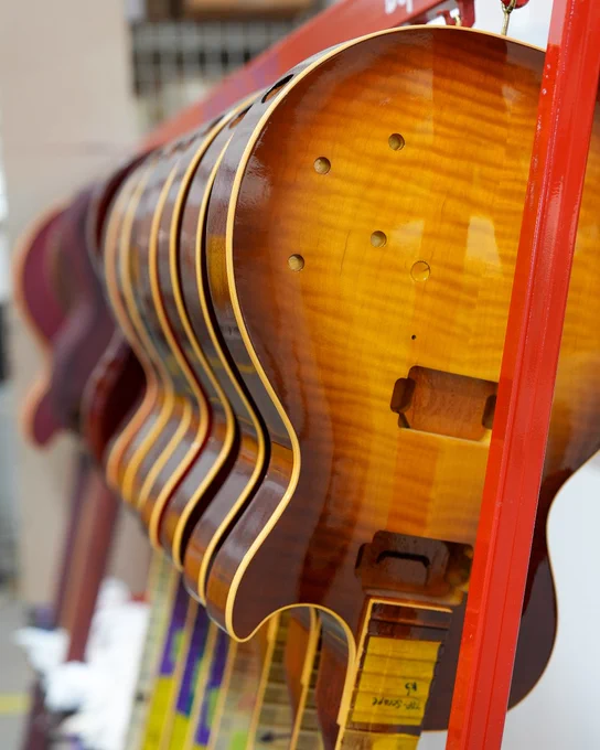 Several Gibson electric guitar bodies are hanging in a row on a red rack, showcasing their wooden finishes and craftsmanship.