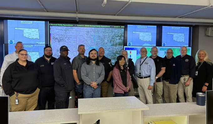 Students from the L101 Foundations of Emergency Management course pose in front of the TV wall at the State Emergency Operations Center.