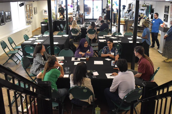 Event attendees sit and talk at two large tables.
