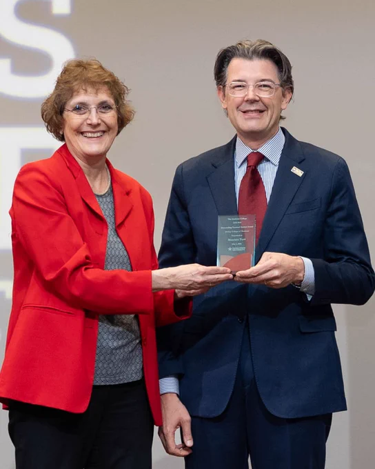 Two professionals in formal attire holding a glass award together during as one presents the award to the other