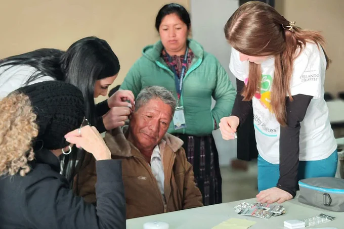 Students fit a hearing aid to a patient's ear during the "Help Guatemala Hear" service trip.