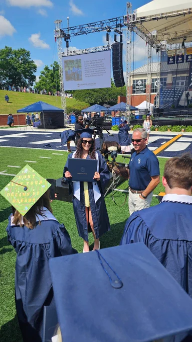 A female graduate poses for a photo with Freedom II, a live bald eagle mascot, at commencement.