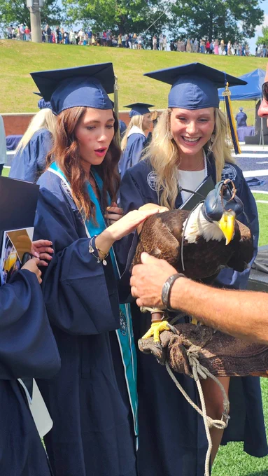 Two female graduates gasp as they pet Freedom II, a live bald eagle mascot.