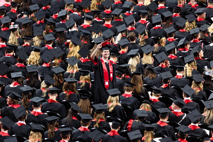 A male graduate stands up and waves amid a sea of seated graduates. (Liz McCue/University Communication and Marketing)