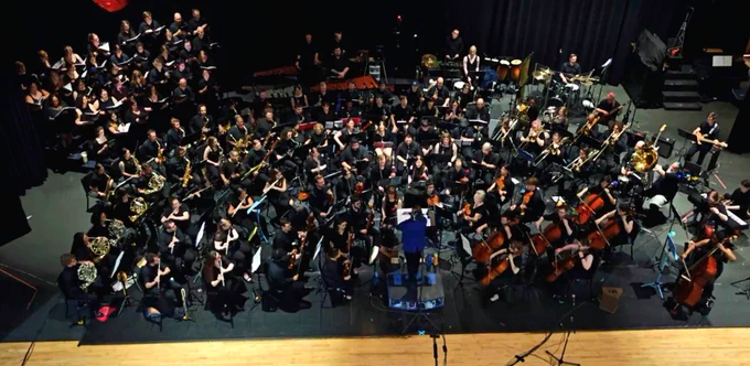 The full orchestra and choir performing, viewed from above. Tad is conducting