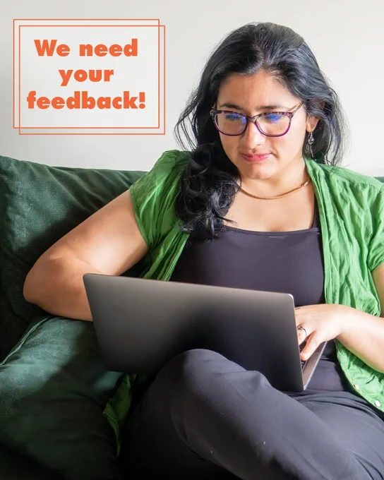 Person sitting on a green couch using a laptop with a sign saying 'We need your feedback!' in orange text.