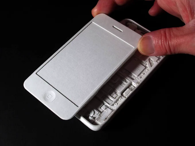 Hand holding a paper-crafted model of a smartphone with the screen being lifted to reveal internal paper components.