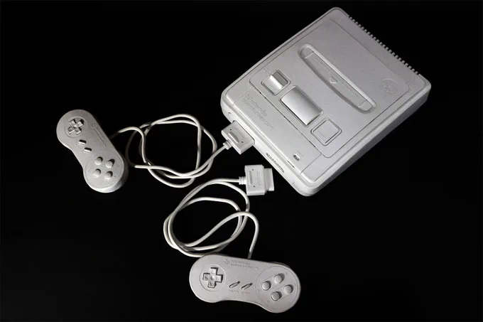 White paper sculpture of a vintage Super Nintendo Entertainment System (SNES) with two wired controllers on a black background.