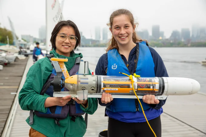 Two students hold an autonomous underwater vehicle on a dock