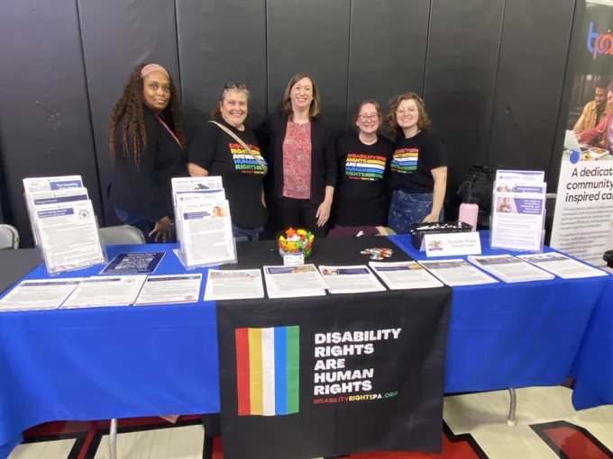 Image of (from left to right) staff attorney Jenee' Oliver, administrative coordinator Stacey Mamas, CEO Jennifer Garman, Director of Intake and Grants Management Shari Mamas, and policy and communications associate Hannah Brown all standing behind DRPs resource table at the disability and mental health summit. 