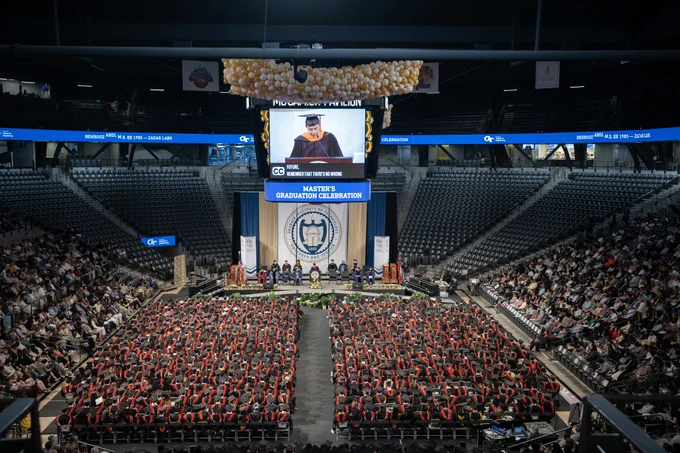 Wide, high-angle view of the Engineering Master's Graduation Celebration in McCamish Pavilion with the floor full of graduates and a speaker on the jumbotron.