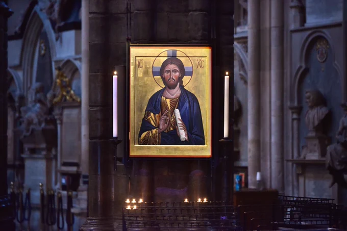 A framed icon of Christ hanging on a pillar in Westminster Abbey, with tall lit white candles burning on either side