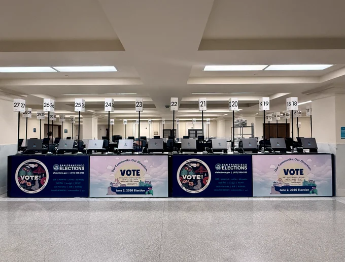 Image of the City Hall Voting Center, including voting booths displaying the text "Vote" and "June 2, 2026, Election" with San Francisco cityscape graphics. 